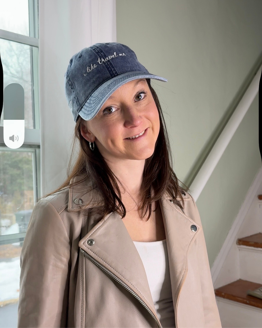 Woman wearing a blue cap with text, standing indoors near a window.