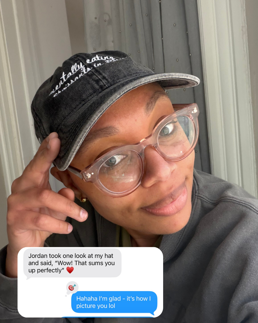 Person wearing travel hat with "mentally eating croissants in Paris", pointing to it, with a text overlay on a neutral background