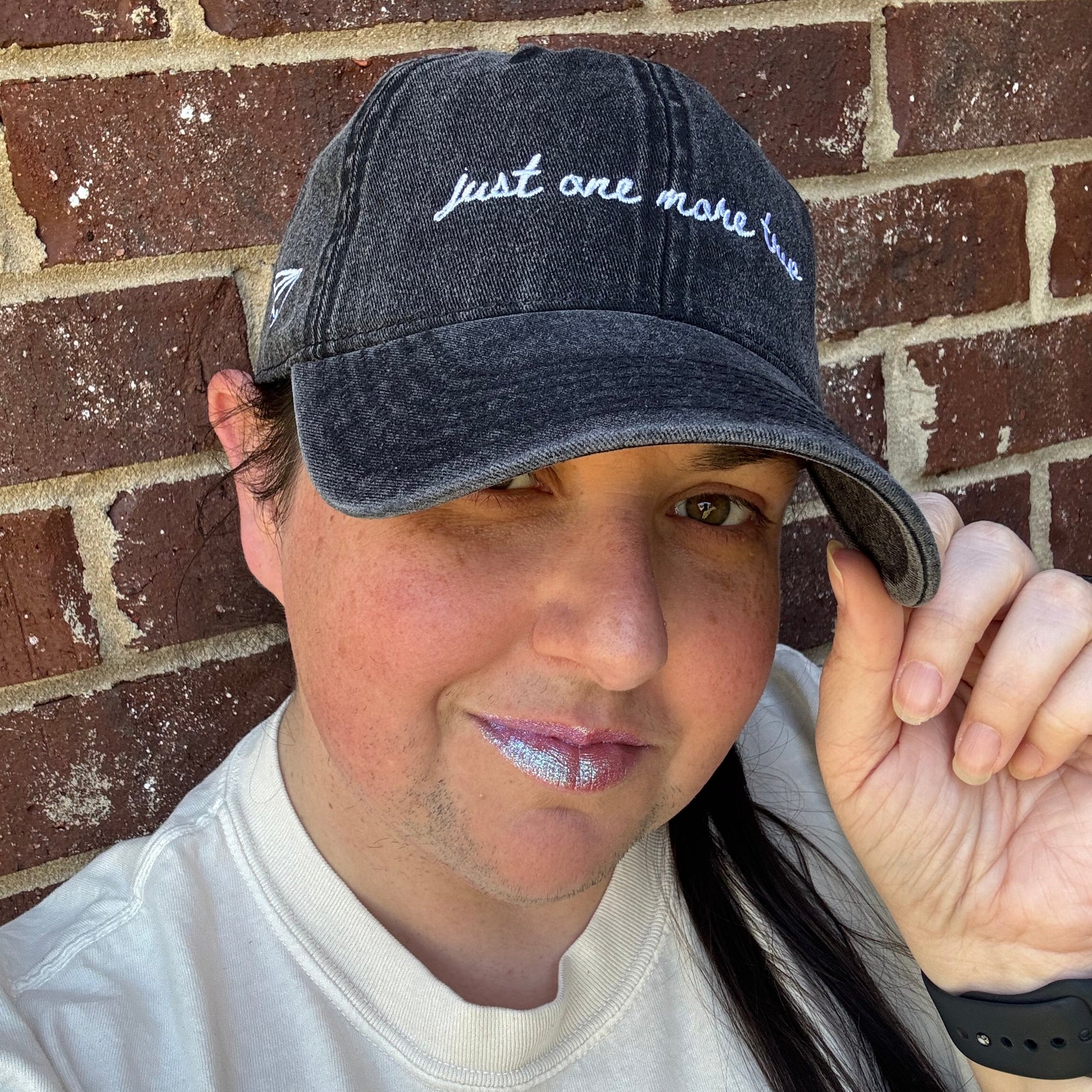 Person wearing a travel themed hat with text "just one more trip"  on a brick surface