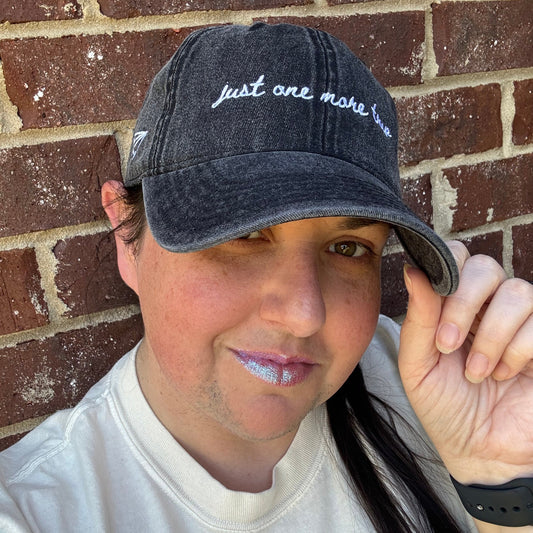 Person wearing a travel themed hat with text "just one more trip"  on a brick surface