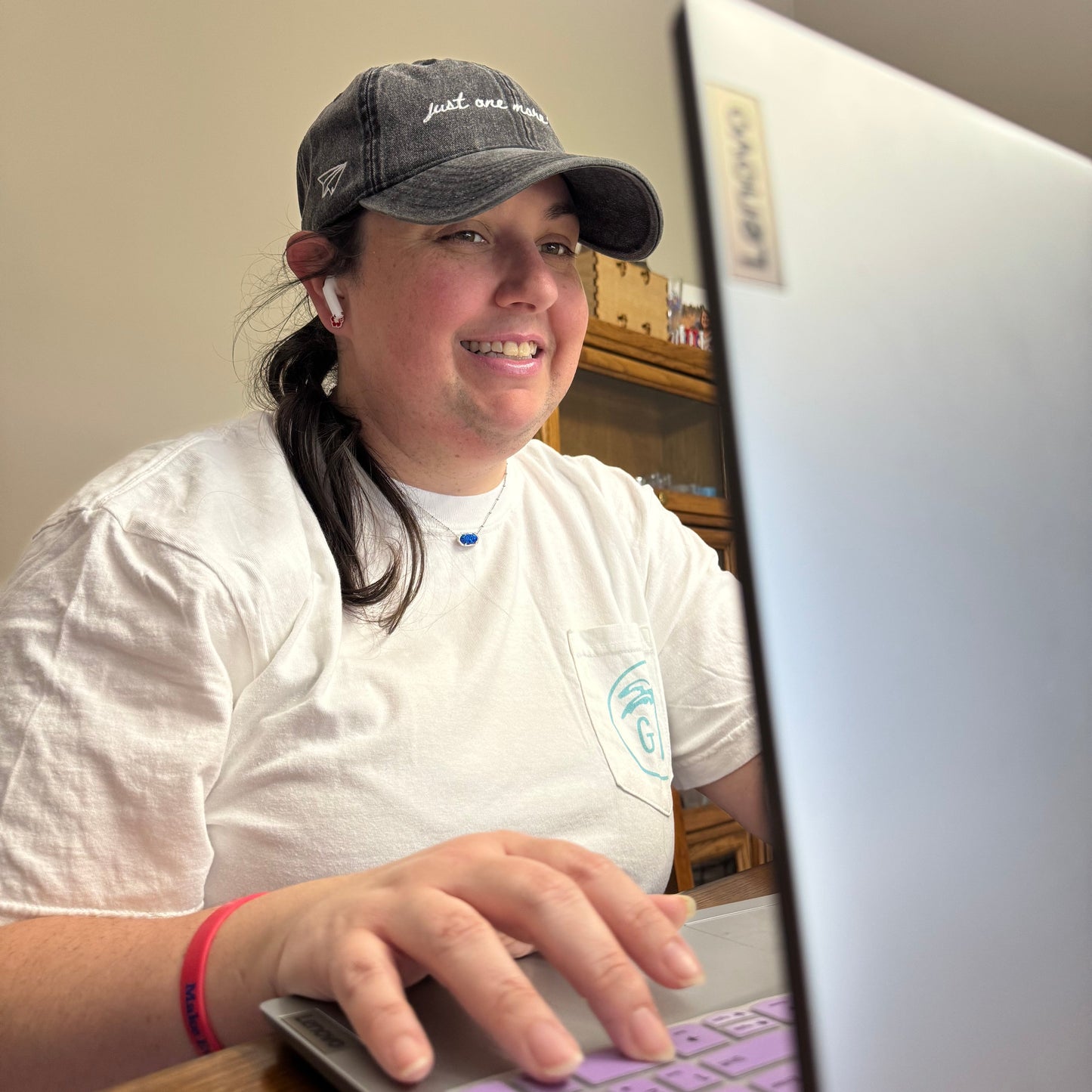 Person using a laptop wearing a black travel hat with words "just one more trip" on it
