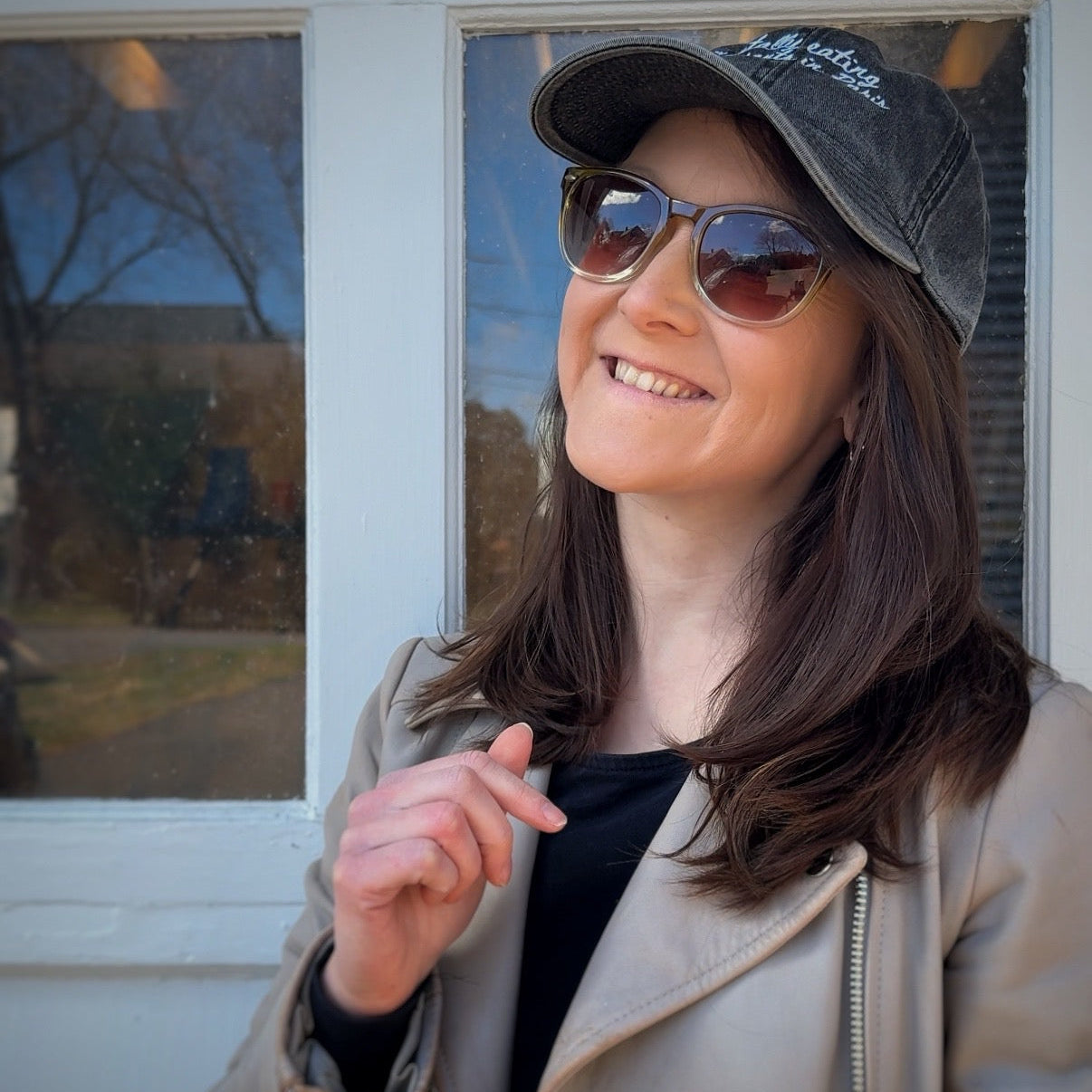 Woman wearing sunglasses and a travel hat with "mentally eating croissants in Paris" standing outdoors with a window in the background