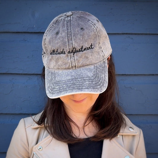 Person wearing a distressed baseball cap with text "altitude adjustment"  against a blue wall