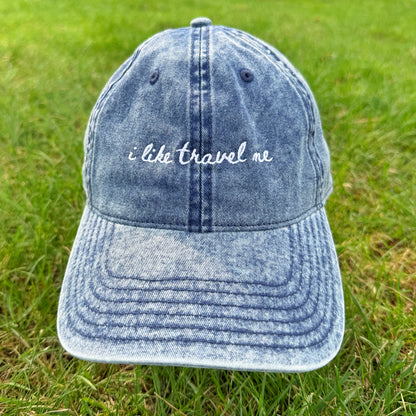 Blue denim cap with 'i like travel me' text on grass