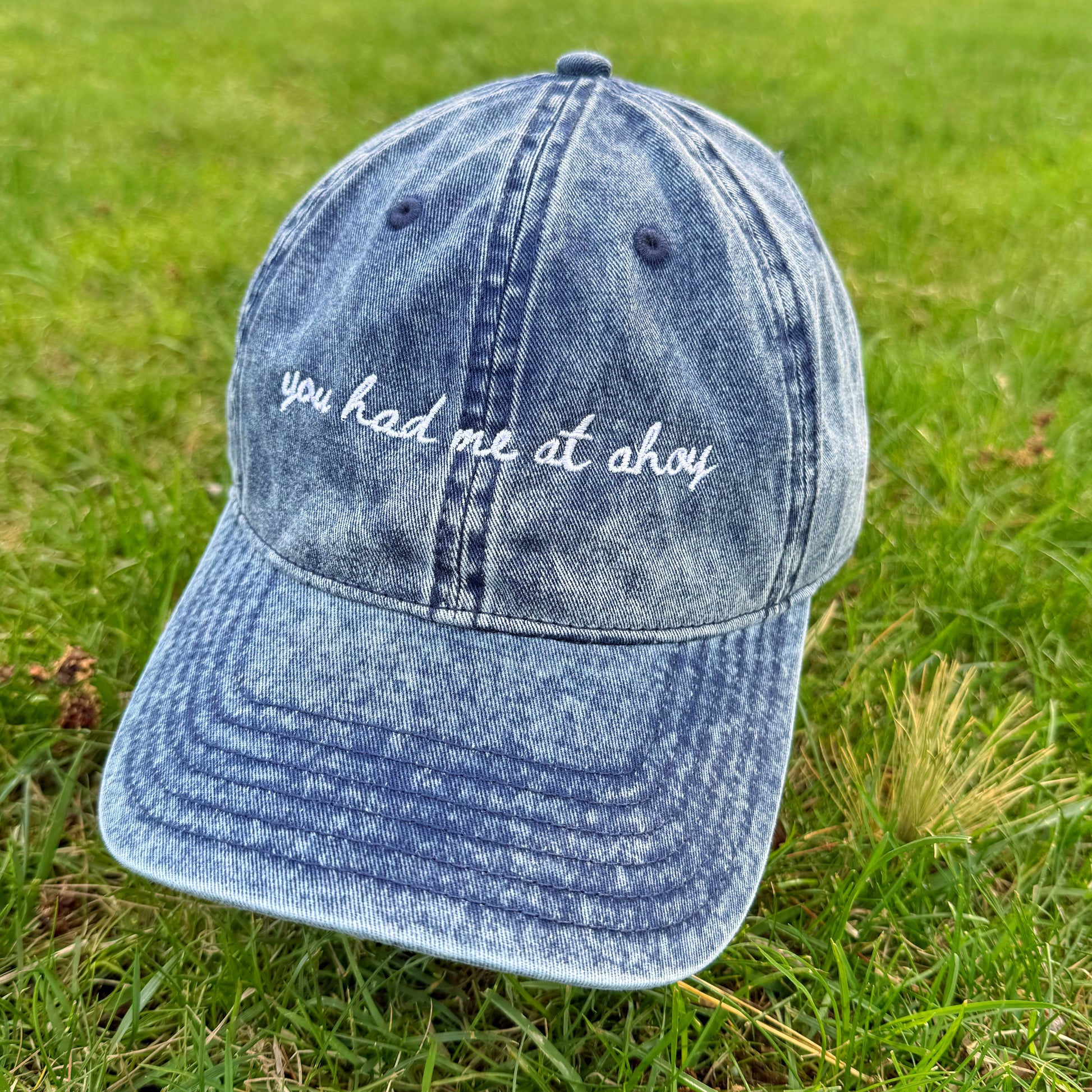 Blue denim cap with 'you had me at ahoy' text on grass