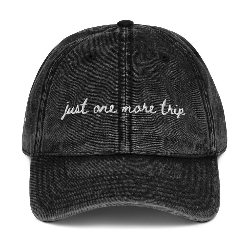 Vintage wash black travel themed hat with words "just one more trip" on it