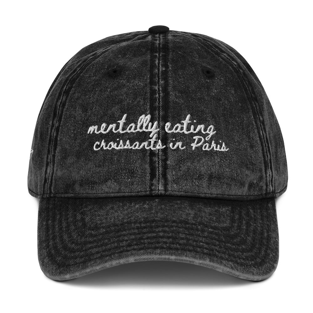 Vintage wash black travel themed hat with the words "mentally eating croissants in Paris"