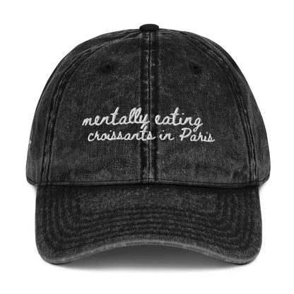 Vintage wash black travel themed hat with the words "mentally eating croissants in Paris"